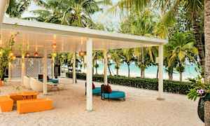 En overdækket terrasse med siddepladser på en sandstrand, omgivet af palmer og med udsigt til havet. (AI-genereret tekst)