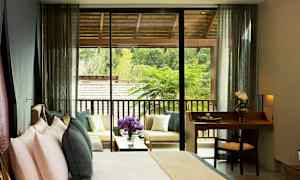 Et hotelværelse med en seng og et lille skrivebord samt en terrasse med siddepladser og udsigt over grønne områder. (AI-genereret tekst)