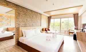 Et rummeligt hotelværelse med en stor seng, sandstensvæg, spejl, sofa og vindue, der fører ud til en balkon. (AI-genereret tekst)