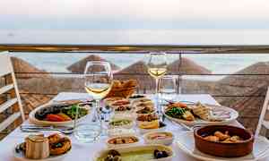 Et opdækket bord med forskellige retter og vinglas, med udsigt over stranden og havet. (AI-genereret tekst)