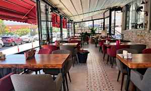 Billede af en restaurant med rødt interiør, træborde og bløde stole. Udsigt over gaden ses gennem glasvinduer. (AI-genereret tekst)