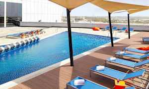 En moderne pool med blåt vand omgivet af liggestole og skyggesejl. (AI-genereret tekst)