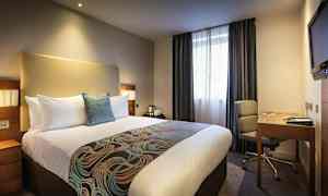 Hotelværelse med en stor seng, skrivebord og stol. (AI-genereret tekst)