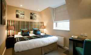 Et hotelværelse med en dobbeltseng med stribet sengegavl og to natborde med lamper. Et skrivebord med stol ved et vindue. (AI-genereret tekst)