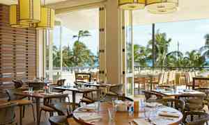 En restaurant med udendørs servering og udsigt over palmer og havet. (AI-genereret tekst)