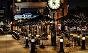 En udendørs servering ved en restaurant eller hotel med skilt og ur, aftenbelysning. (AI-genereret tekst)