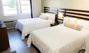 Et hotelværelse med to hvide senge og farverige puder. (AI-genereret tekst)