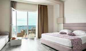 Et hotelværelse med en stor seng, glasdøre til en balkon og udsigt over havet. (AI-genereret tekst)