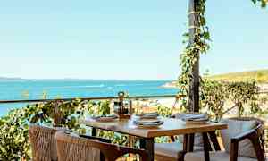 Udendørsservering med bord og stole ved havet. (AI-genereret tekst)