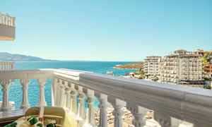 Udsigt fra en balkon mod havet, omgivet af lejlighedskomplekser og en strand. (AI-genereret tekst)