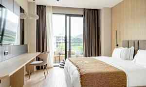 Et hotelværelse med en seng, skrivebord, stol og en altandør med udsigt. (AI-genereret tekst)