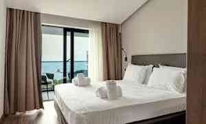 Et hotelværelse med en opredt seng og adgang til en balkon med havudsigt. (AI-genereret tekst)