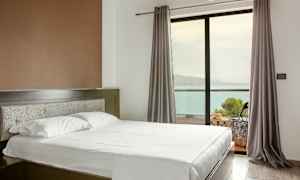 Et hotelværelse med en seng, et vindue med gardiner og udsigt over havet. (AI-genereret tekst)