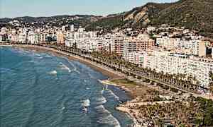 Udsigt over en by ved stranden med høje bygninger og havet i forgrunden. (AI-genereret tekst)