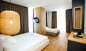 Et hotelværelse med to senge, en hængende lampe, et vægmonteret tv og et skrivebord med en kaffemaskine. (AI-genereret tekst)