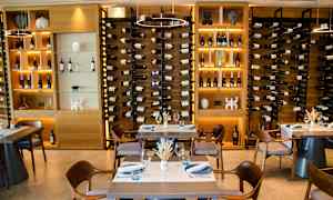 Vinflasker arrangeret i hylder bag spiseborde. (AI-genereret tekst)