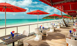 Udendørs serveringsområde med røde parasoller ved en sandstrand. (AI-genereret tekst)