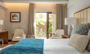 Et lyst og moderne soveværelse med en seng med hvidt og blåt sengetøj, to stole og et lille bord ved en glasdør med udsigt til en have. (AI-genereret tekst)