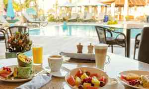 Morgenmad med grøntsagswrap, frugtsalat og drikkevarer ved et udendørs poolområde. (AI-genereret tekst)