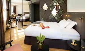 Et hotelværelse med en stor seng, vægdekorationer og et spejl, der reflekterer rummet. En kuffert står ved siden af, og der er en lille kaktus på et bord. (AI-genereret tekst)