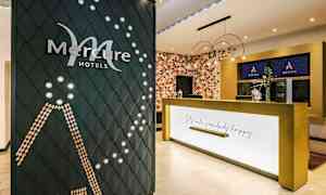 Receptionen på et Mercure-hotel med virksomhedens logo synligt på en dekorativ væg og en reception med teksten "Let's make somebody happy". (AI-genereret tekst)