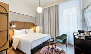 Et hotelværelse med en dobbeltseng, en stol og et bord samt et stort vindue med gardiner. (AI-genereret tekst)