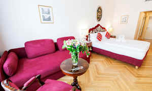 Et hotelværelse med en rød sofa, et rundt bord med en blomsterbuket og en seng med røde detaljer. (AI-genereret tekst)