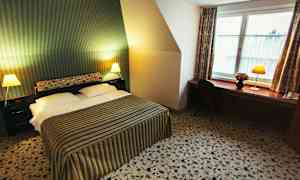 Et hotelværelse med en dobbeltseng, stribet sengetæppe, to natborde med lamper og en arbejdsbænk med stol ved et vindue. (AI-genereret tekst)