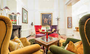 En stilfuldt indrettet lounge med farverige lænestole og sofaer omkring et bord. Væggene er dekoreret med kunst, og en pejs med pynt ses på siden. (AI-genereret tekst)