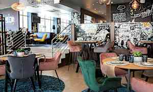 En moderne indretning af en restaurant med farverige stole omkring borde med dækkede tallerkener og glas. Væggene er dekoreret med kunstneriske mønstre og tekster. (AI-genereret tekst)