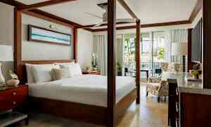 Et elegant soveværelse med en himmelseng, siddepladser og udsigt over grønne områder gennem åbne glasdøre. (AI-genereret tekst)