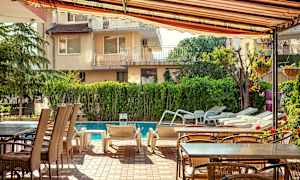 Udendørs møbler og liggestole ved en pool, omgivet af grønt og bygninger. (AI-genereret tekst)