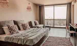 Et lyst og moderne hotelværelse med seng, sofa og en altan med havemøbler. (AI-genereret tekst)