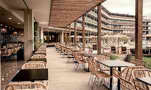 En udendørs restaurant med rottingmøbler og udsigt over en pool og solsenge. (AI-genereret tekst)