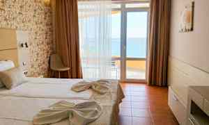 Et hotelværelse med en dobbeltseng opredt med hvide lagner og dekoreret med håndklæder. Der er et vindue med udsigt til havet. (AI-genereret tekst)