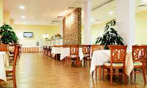 Billede af en spisesal med borde og stole i træ, hvide duge, planter og en buffetsektion. (AI-genereret tekst)