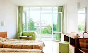 Hotelværelse med dobbeltsenge, skrivebord og åbent vindue ud til en balkon med udsigt. (AI-genereret tekst)