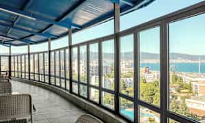 Interiør med en indglaset veranda med udsigt over en by og havet. (AI-genereret tekst)