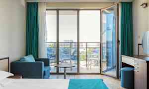 Moderne hotelværelse med en seng, siddeområde og glasdøre ud til en balkon. (AI-genereret tekst)