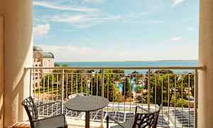 Udsigt fra en balkon mod havet, med stole og bord i forgrunden. (AI-genereret tekst)