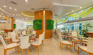 Et restaurantinteriør med flere borde og stole, dekorative vægpaneler med grønt og store glasvægge. (AI-genereret tekst)