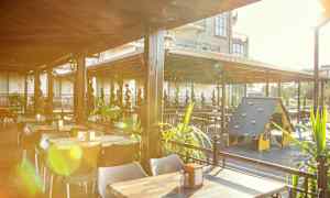 En udendørs restaurant med borde, stole og en legeplads til børn under et tag. (AI-genereret tekst)