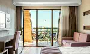 Et lyst hotelværelse med balkon, møbleret med seng, sofa og skrivebord. (AI-genereret tekst)