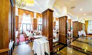 En elegant restaurant med dækkede borde, mørke trægulve og store vinduer med gardiner. (AI-genereret tekst)