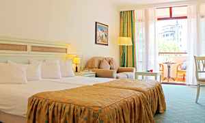 Et hotelværelse med en dobbeltseng, siddeområde med lænestol og bord samt en balkon med møbler og udsigt. (AI-genereret tekst)