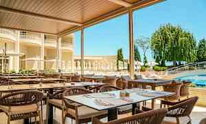 Udendørsrestaurant med borde og stole under tag, omgivet af grønt og en pool i baggrunden. (AI-genereret tekst)