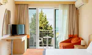 Et hotelværelse med altan, seng, lænestol og TV. (AI-genereret tekst)