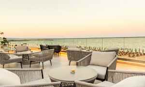 Udsigt over møbleret terrasse med siddepladser og hav i baggrunden. (AI-genereret tekst)