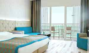 Hotelværelse med dobbeltseng, sofa og balkon med udsigt over havet. (AI-genereret tekst)