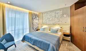 Et hotelværelse med en dobbeltseng, blåt sengetæppe og dekorativ væg bag sengen. (AI-genereret tekst)